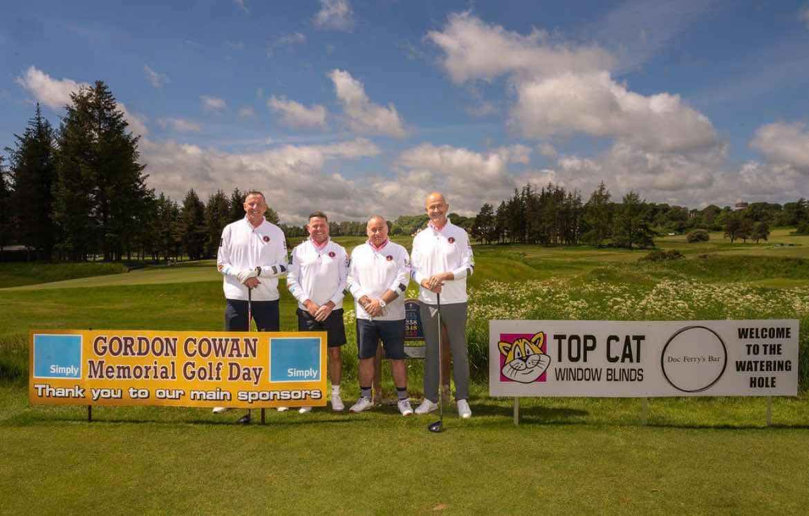 Four golfers in white shirts beside the event banners