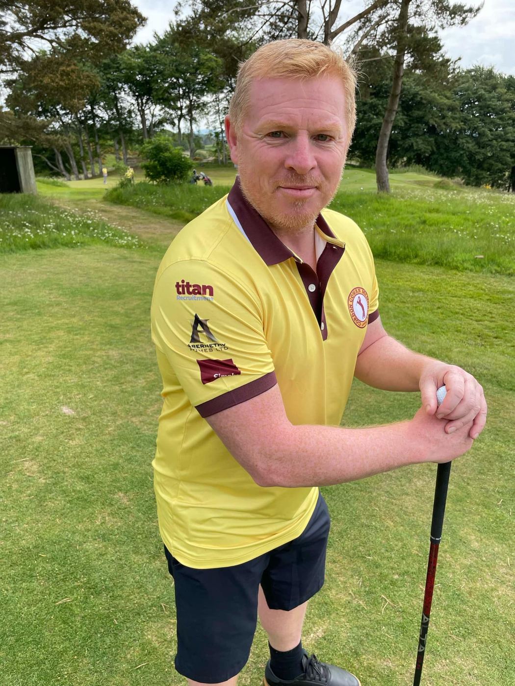 A golfer in a yellow shirt leaning on his club