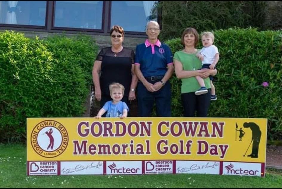 A family standing behind the Gordon Cowan Memorial Golf Day banner